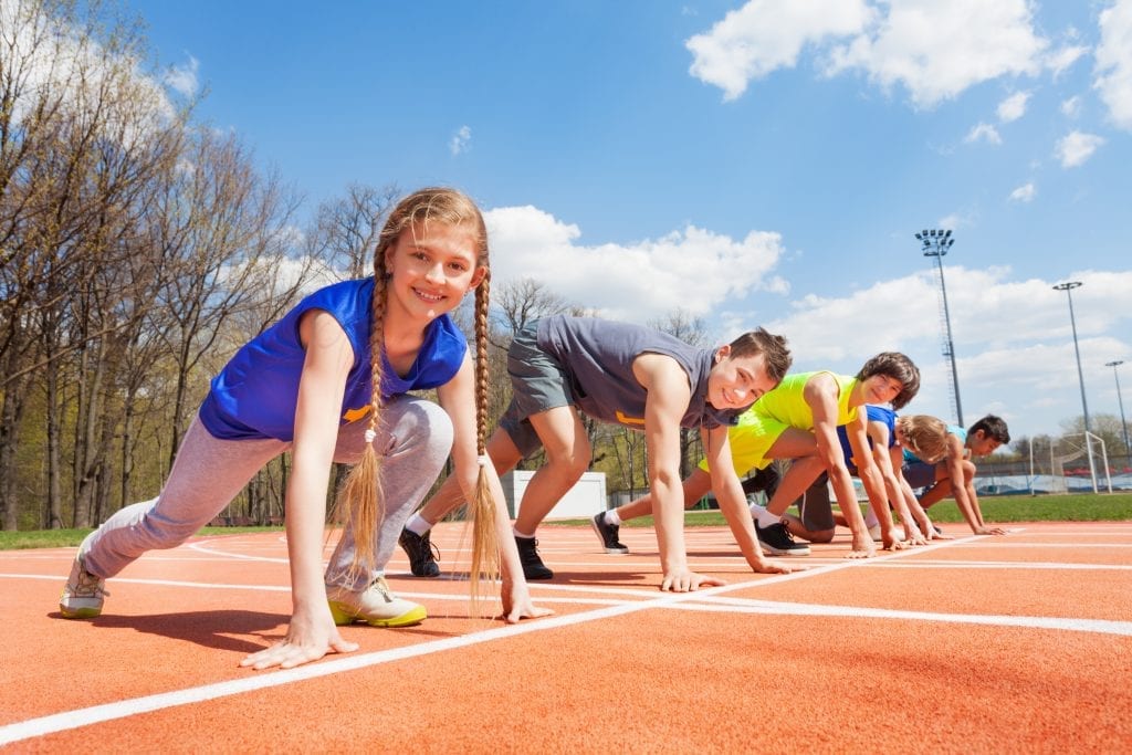 Side view of five teenage sprinters in sportswear lined up ready to race at the stadium