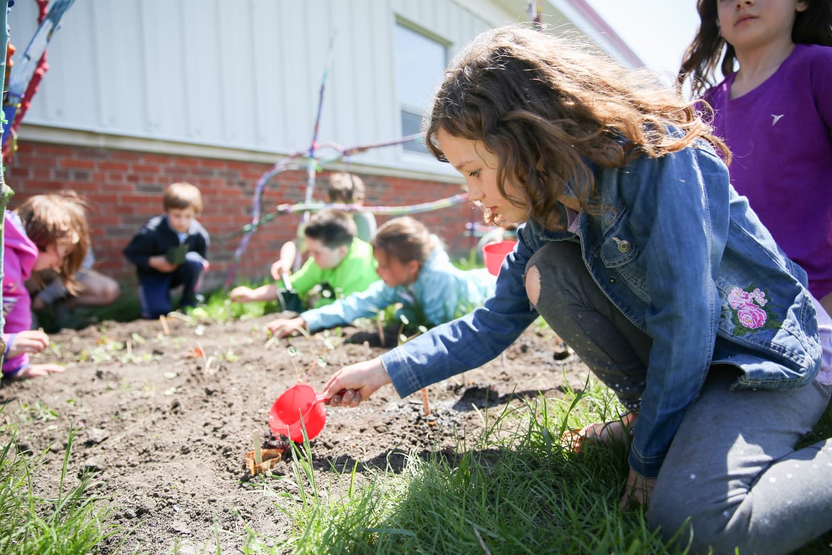 A student waters a garden bed during a nature play workshop.