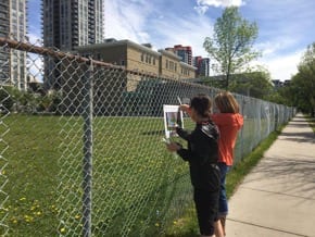 Two people hang a poster with an image from a storybook on a fence.