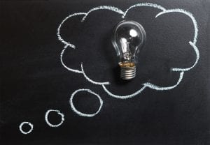 A blackboard with a lightbulb placed on it and a chalk drawing of a thought bubble around the bulb to indicate a thought or idea.