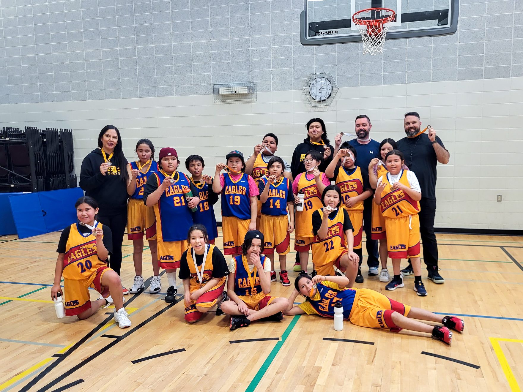 A basketball team wearing gold and blue post with medals. Taken during an Everybody Plays Leagues of Play event.