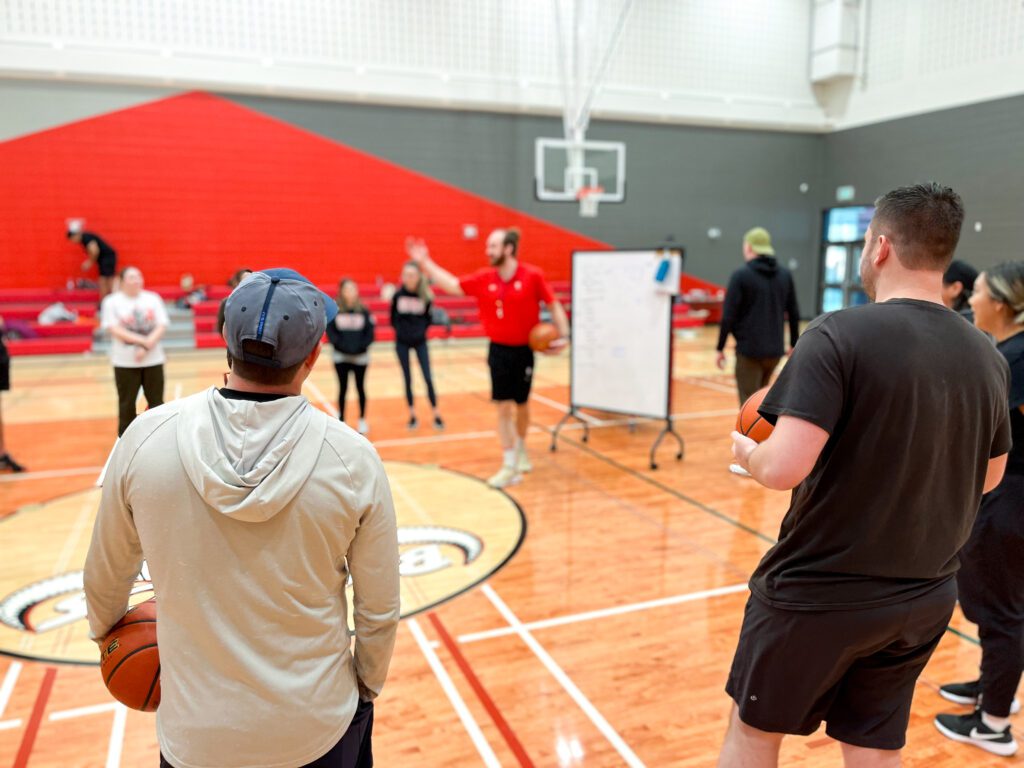 A circle of adults during a basketball coaching clinic with a rolling whiteboard in the centre.