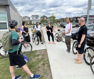 A group of people with bicycles stand in a circle during a consultation meeting in Leduc.