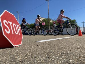 A stop sign in the foreground with three young cyclists in the background at a active school travel event.