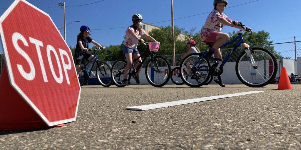 A stop sign in the foreground with three young cyclists in the background at a active school travel event.
