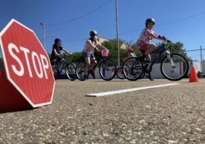 A stop sign in the foreground with three young cyclists in the background at a active school travel event.