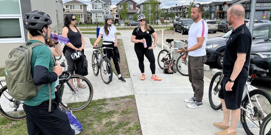 A group of people with bicycles stand in a circle during a consultation meeting in Leduc.