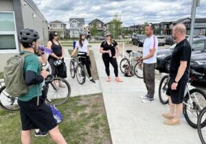 A group of people with bicycles stand in a circle during a consultation meeting in Leduc.