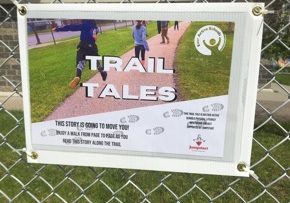 A laminated, corrugated plastic board with an image on it that says "Trail Tales". This is the introductory page to inform passersby of the purpose of the Trail Tales project.