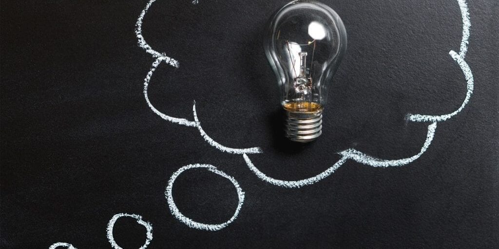 A blackboard with a lightbulb placed on it and a chalk drawing of a thought bubble around the bulb to indicate a thought or idea.